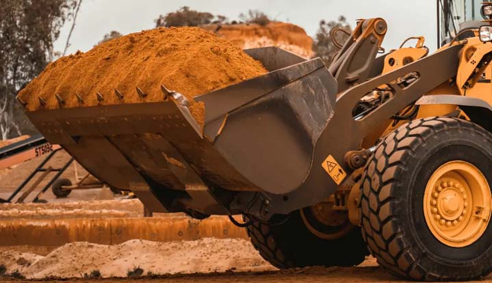 Primer plano de la pala cargadora de una retroexcavadora llevando tierra.